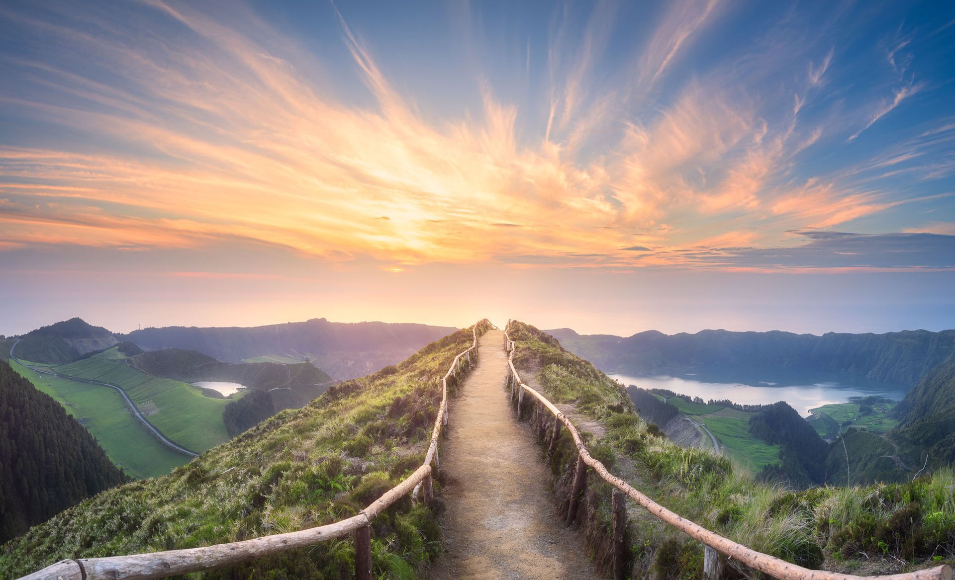 A path going up a hill with a wooden fence and a sunset in the background.