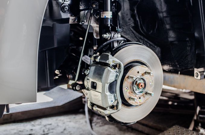 Primo piano del disco e della pinza del freno anteriore di un'auto all'interno del passaruota durante la riparazione.