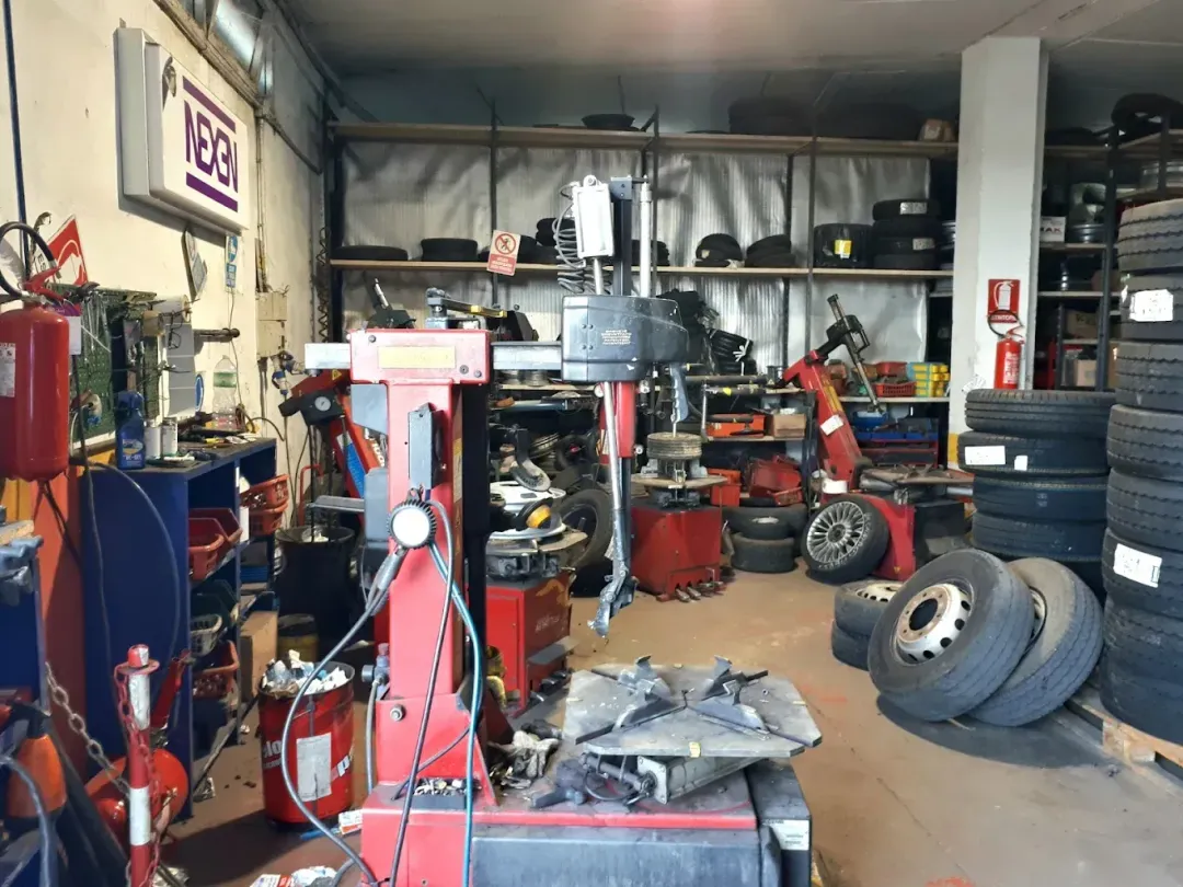 Luminosa sala d'attesa di un'officina meccanica con insegna Goodyear, sedie blu, riviste e poster alle pareti.