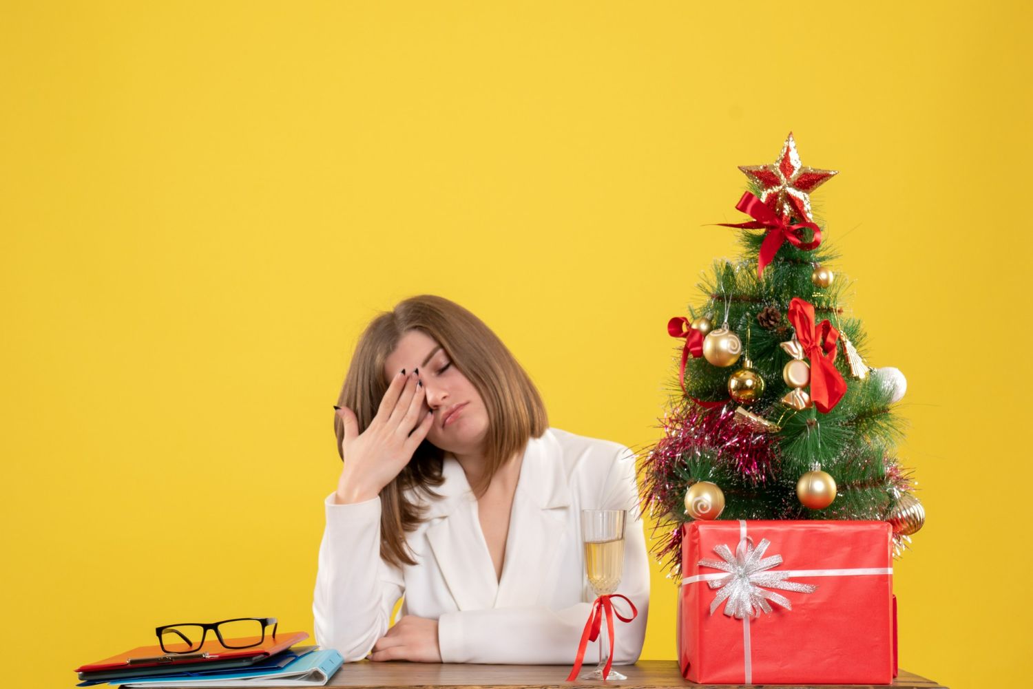 A woman is sitting at a desk with a christmas tree in the background.