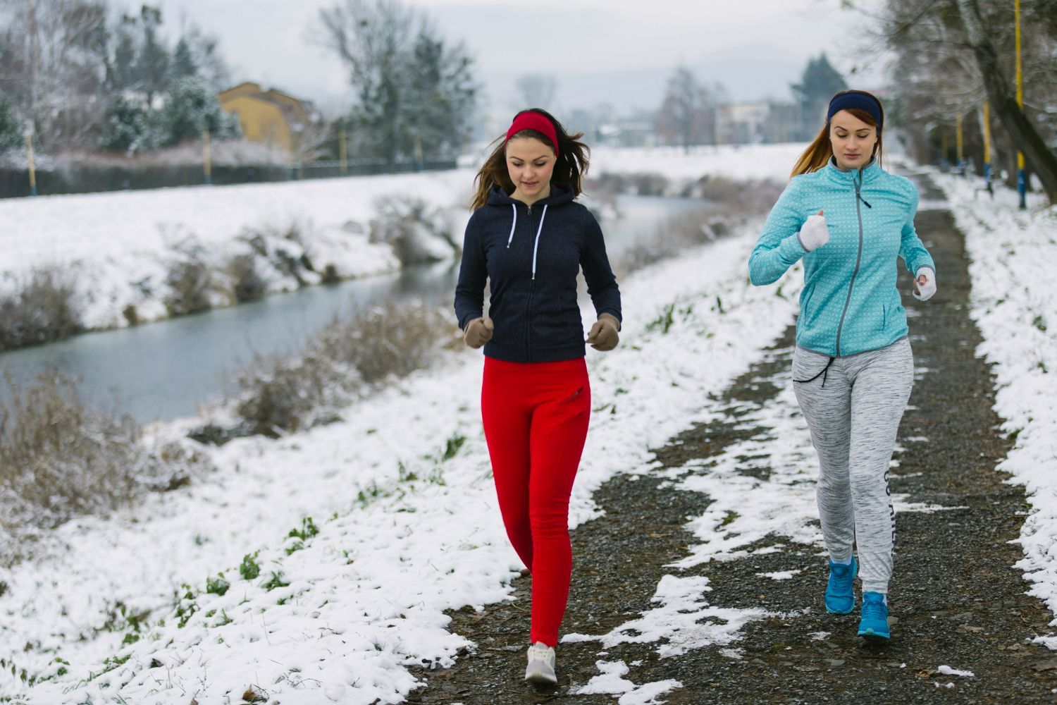 Two women are running in the snow on a path.