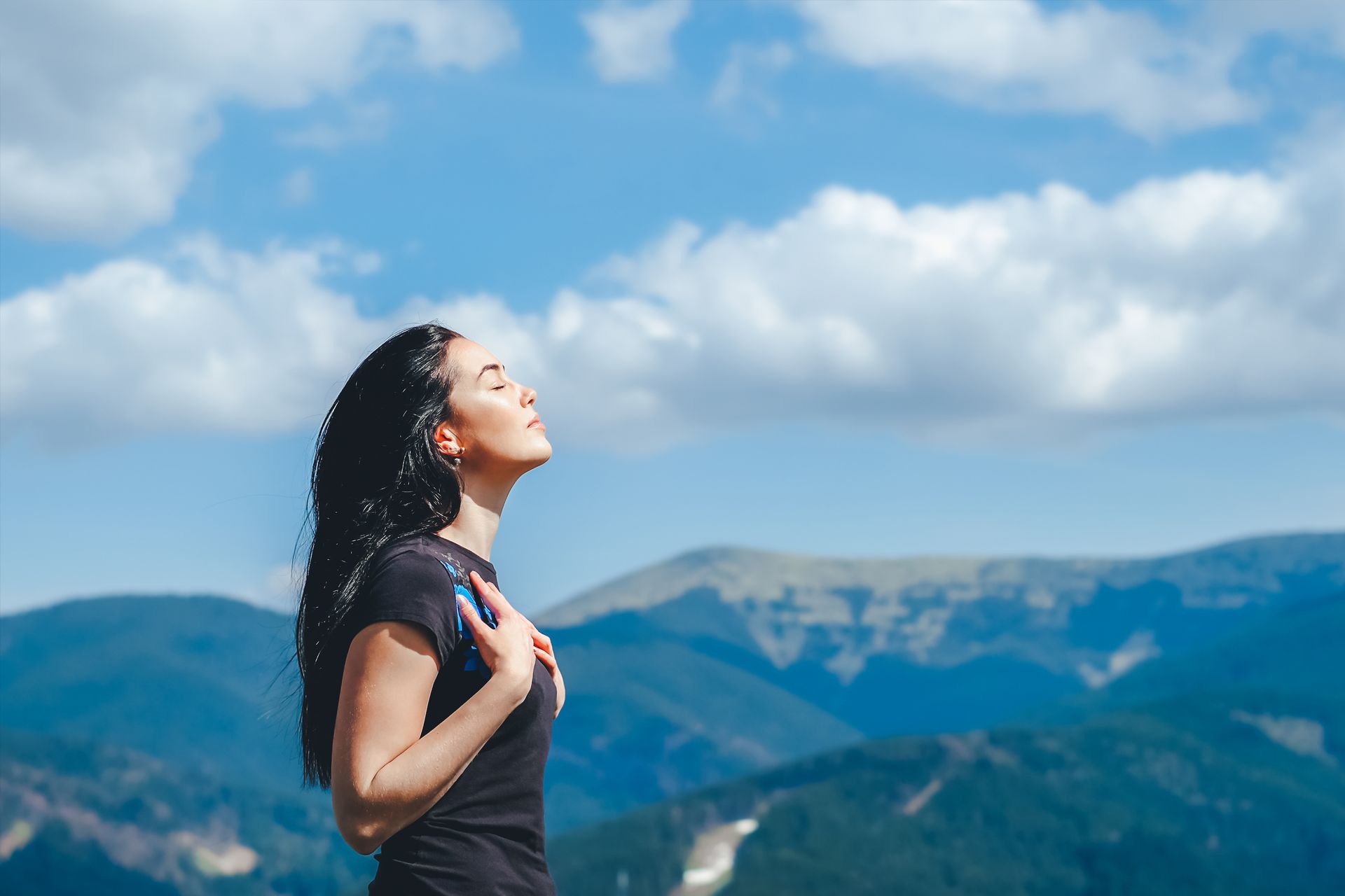 a woman is standing on top of a mountain with her eyes closed .