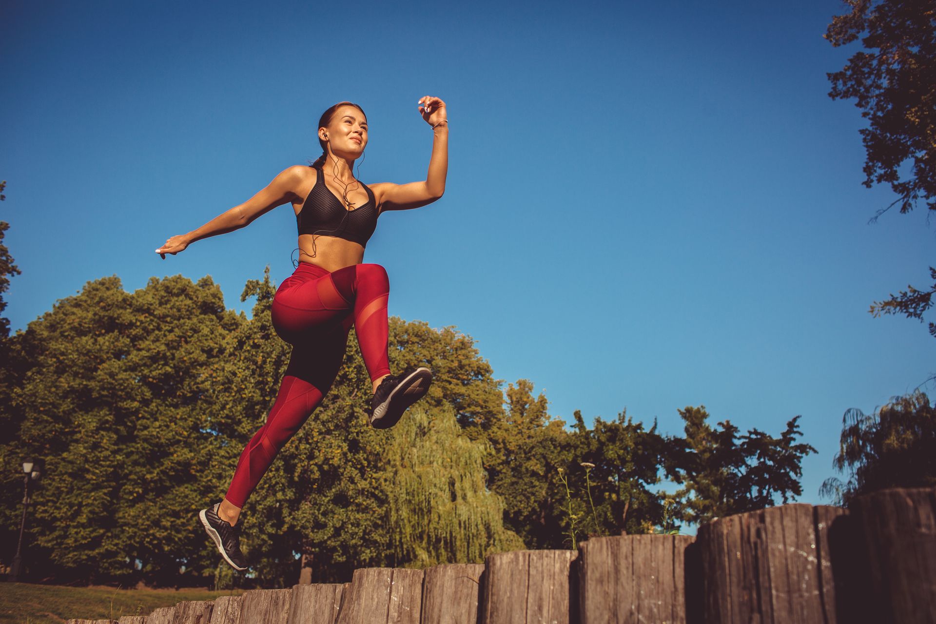 a woman is jumping over a wooden fence in a park .