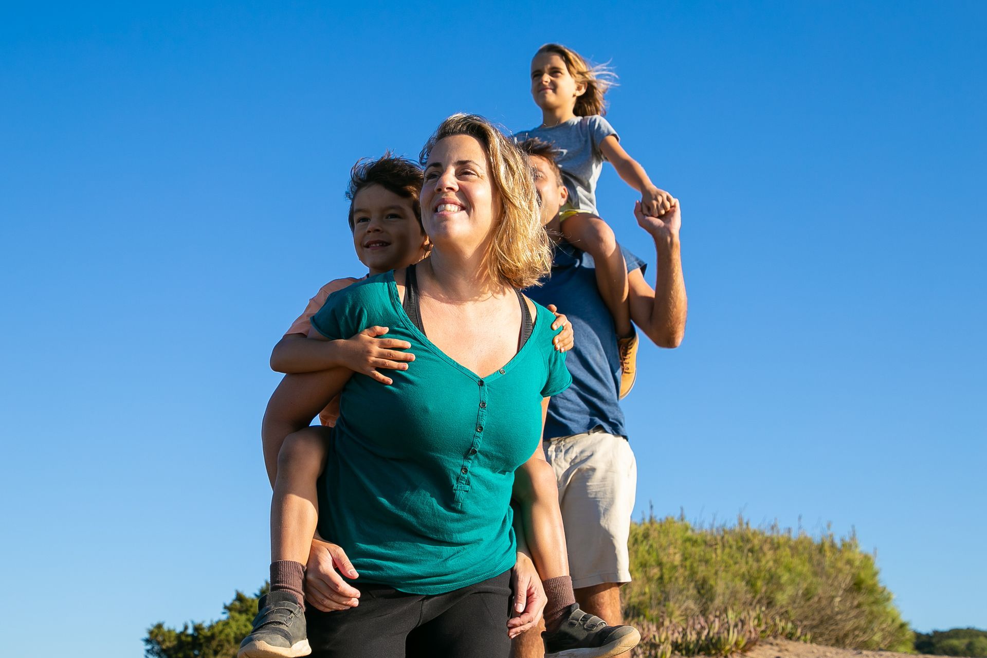 a woman in a green shirt is carrying two children on her shoulders