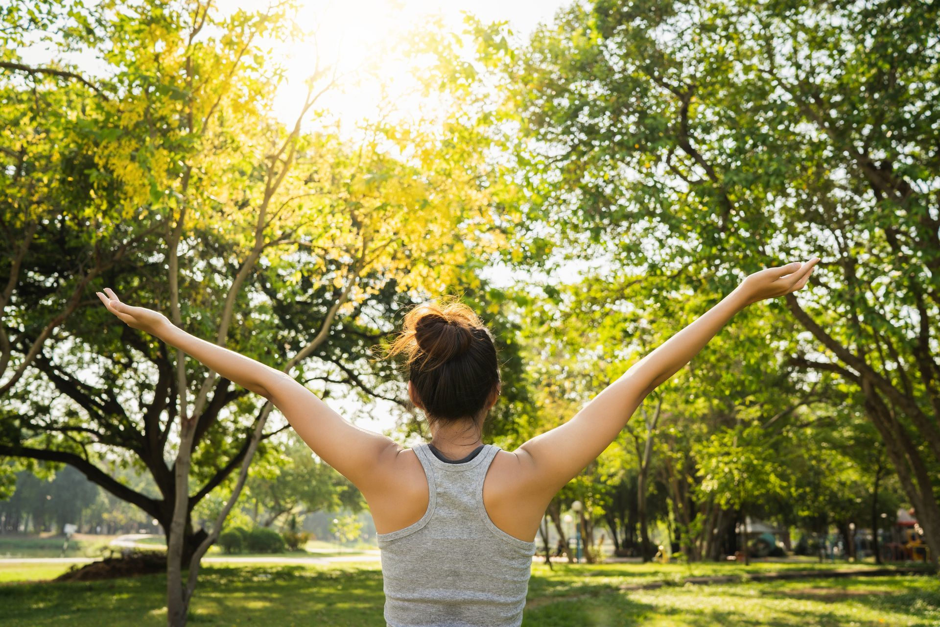 A woman is standing in a park with her arms outstretched.