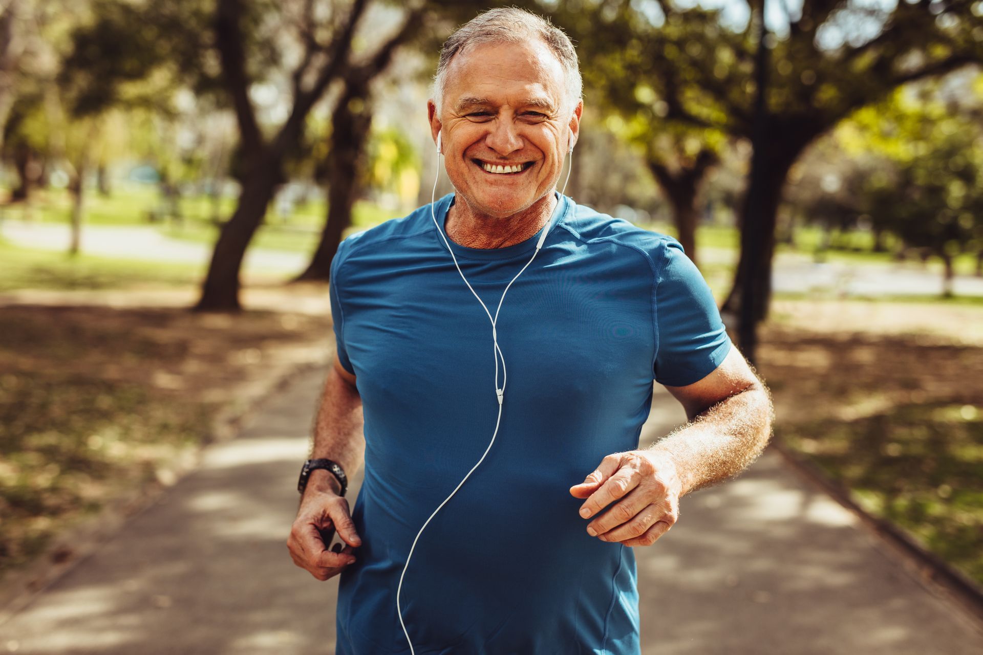 an older man is wearing headphones and smiling while running in a park .