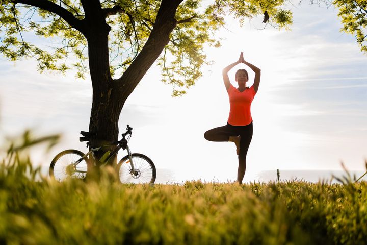 a woman is doing yoga under a tree next to a bicycle .
