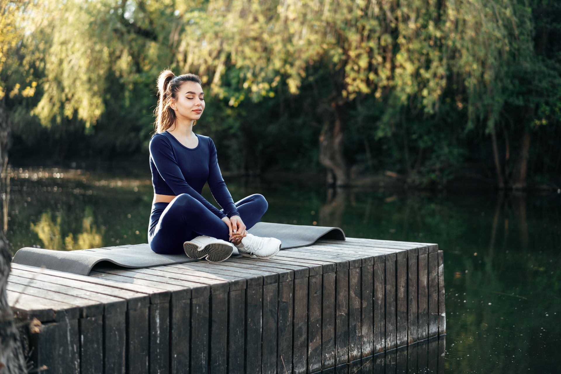 a woman is sitting on a yoga mat on a dock next to a lake .