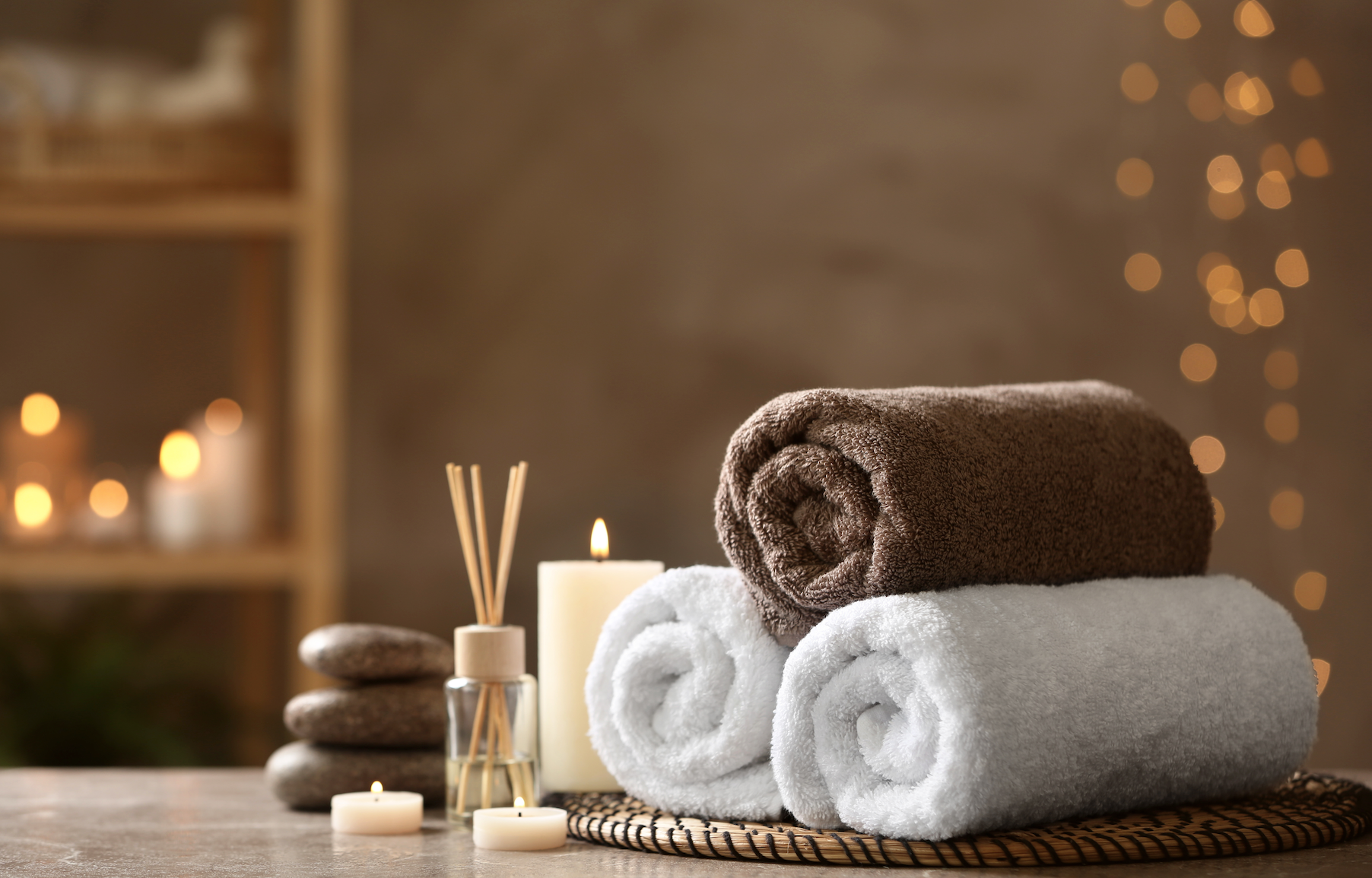A stack of towels , candles , and rocks on a table in a spa.