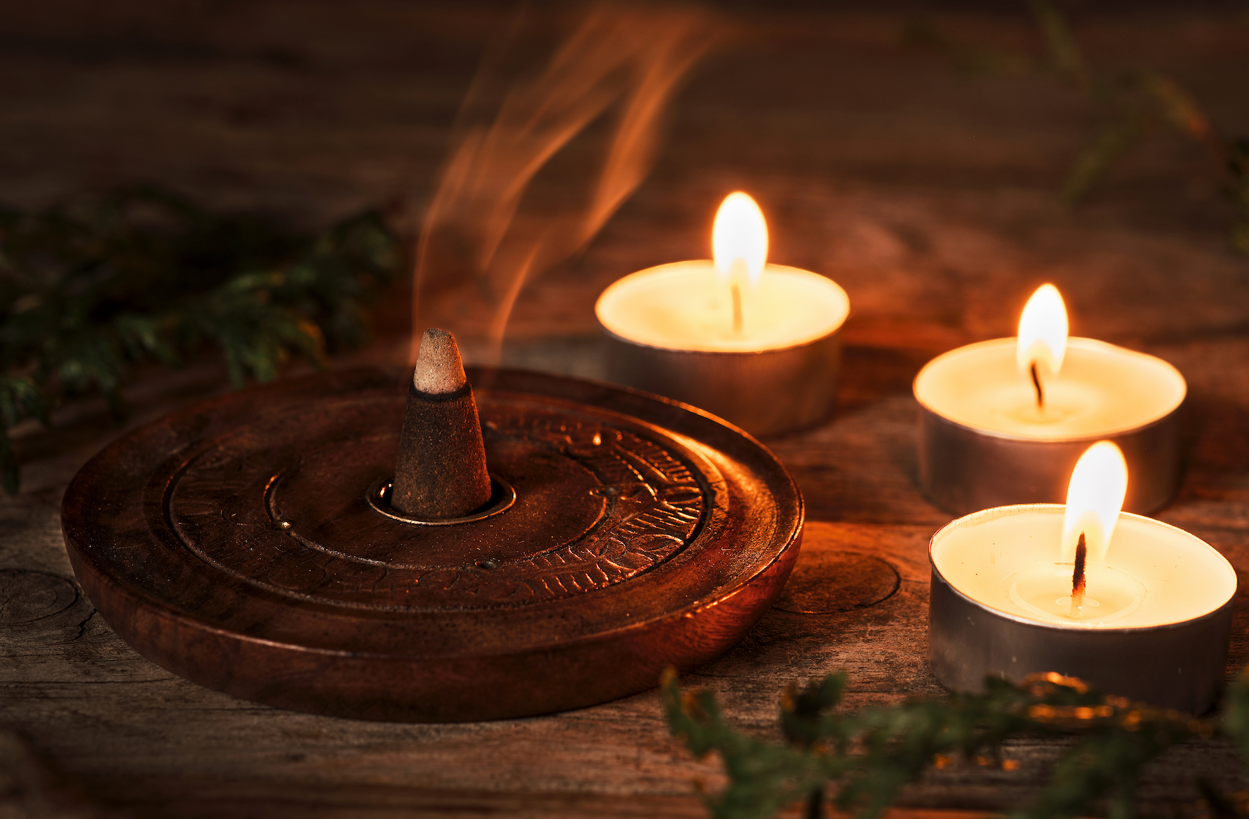 A wooden incense burner with three lit candles on a wooden table.