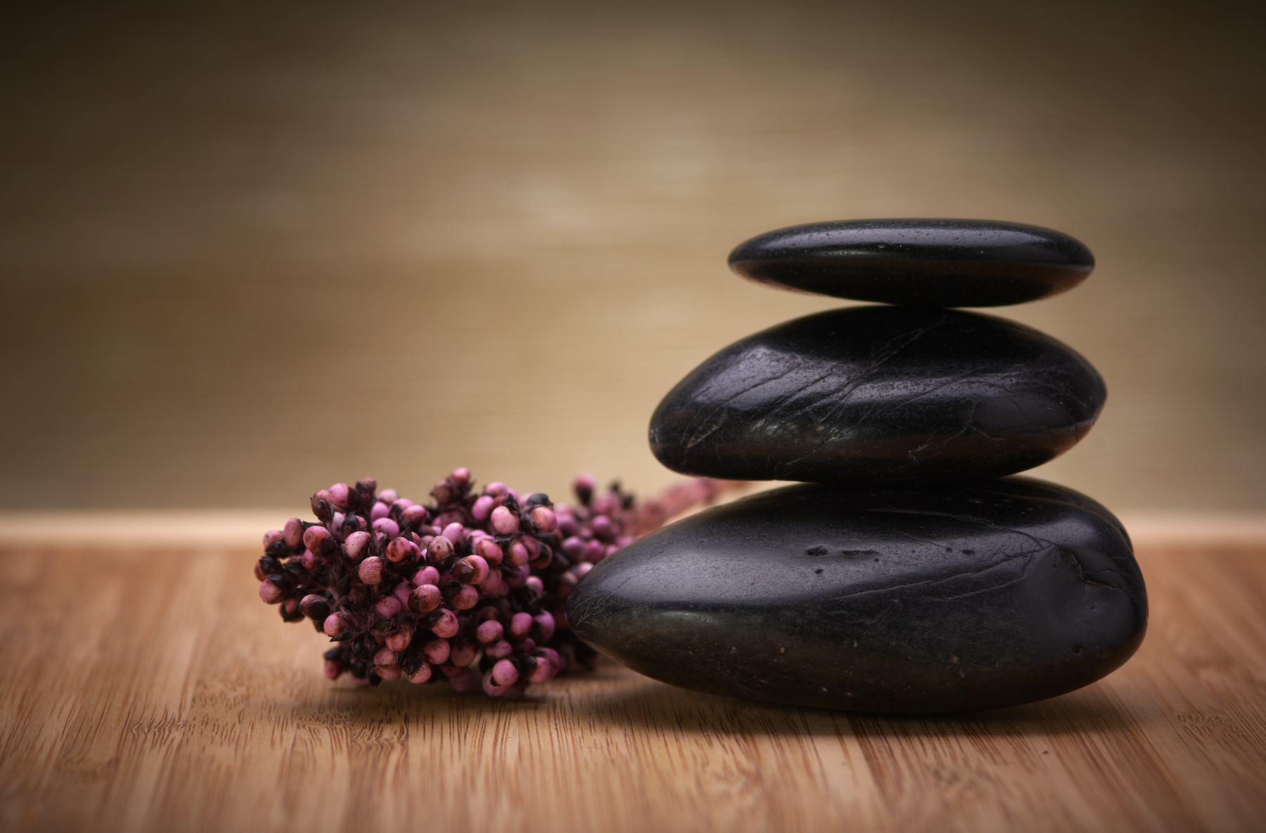 Three black rocks are stacked on top of each other on a wooden table.