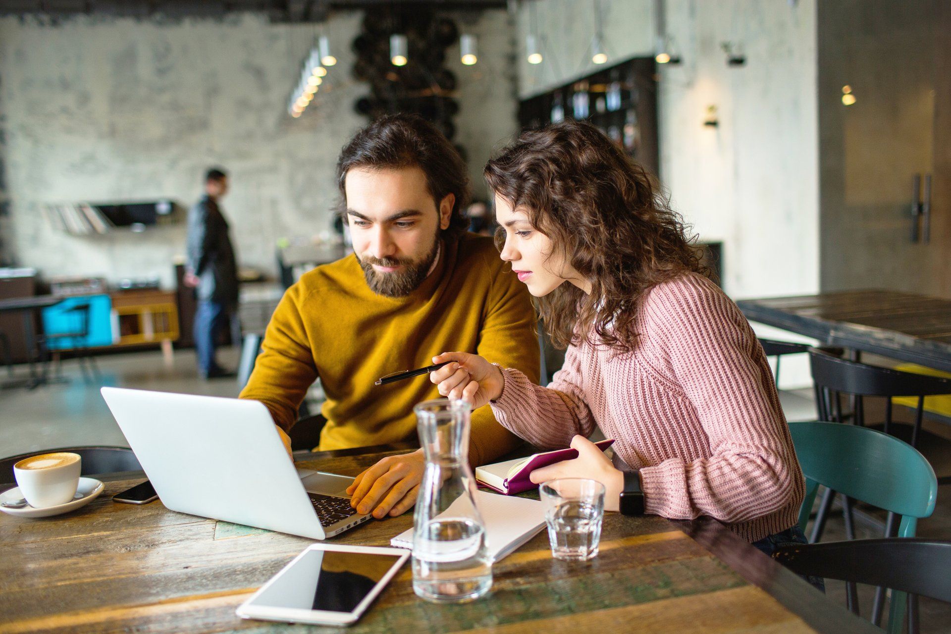 A man and a woman are sitting at a table looking at a laptop.