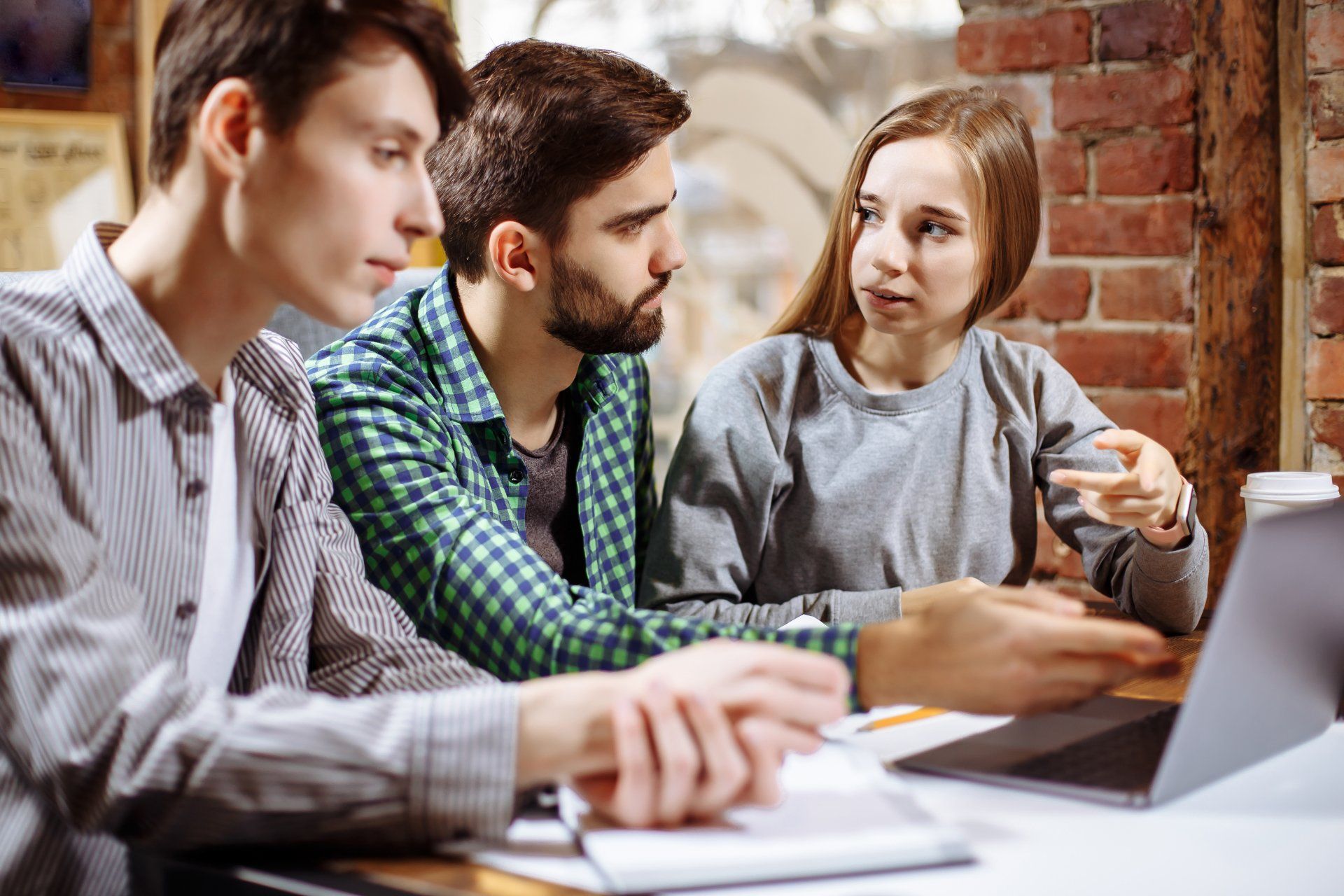 A group of young people are sitting at a table looking at a laptop computer.