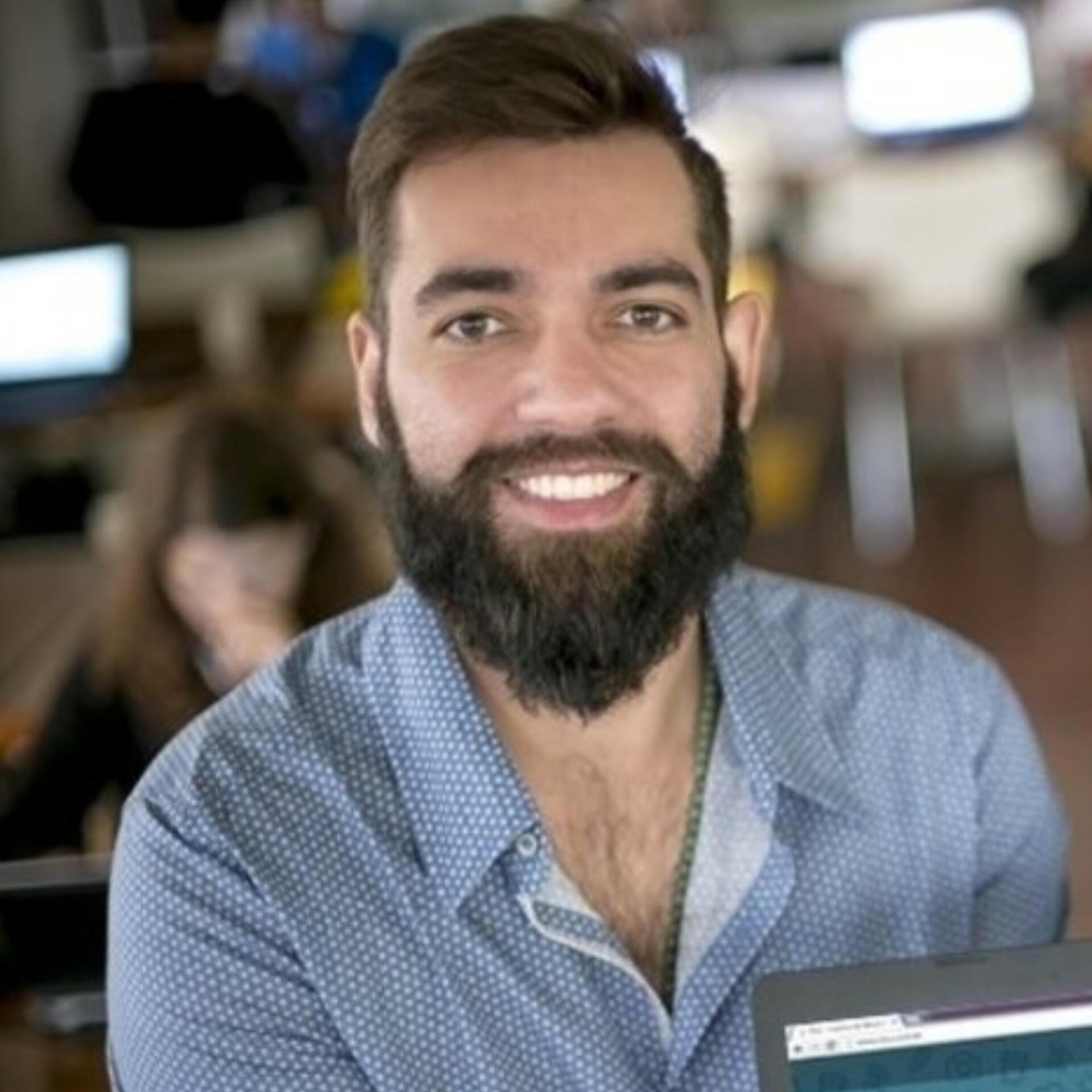 Um homem com barba está sorrindo enquanto segura um laptop.
