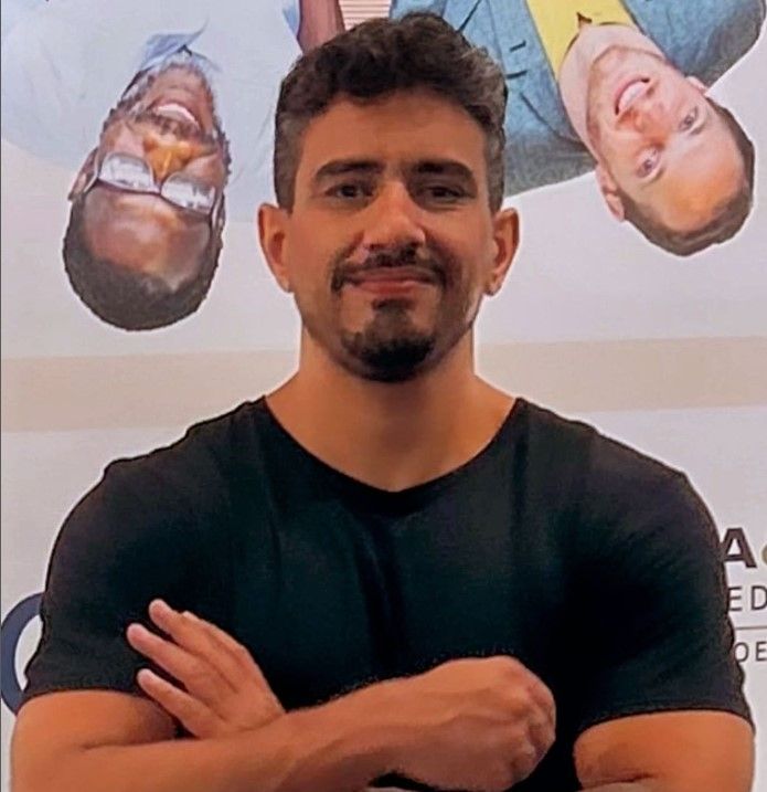 Um homem com os braços cruzados está diante de um pôster de dois homens.