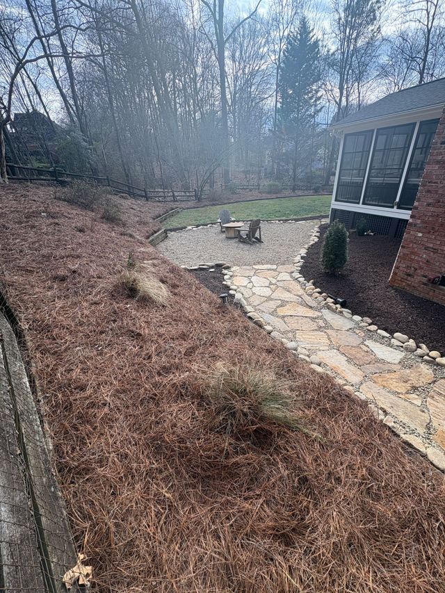 Curved stone walkway beside a house, bordered by mulch and winter trees in a wooded yard