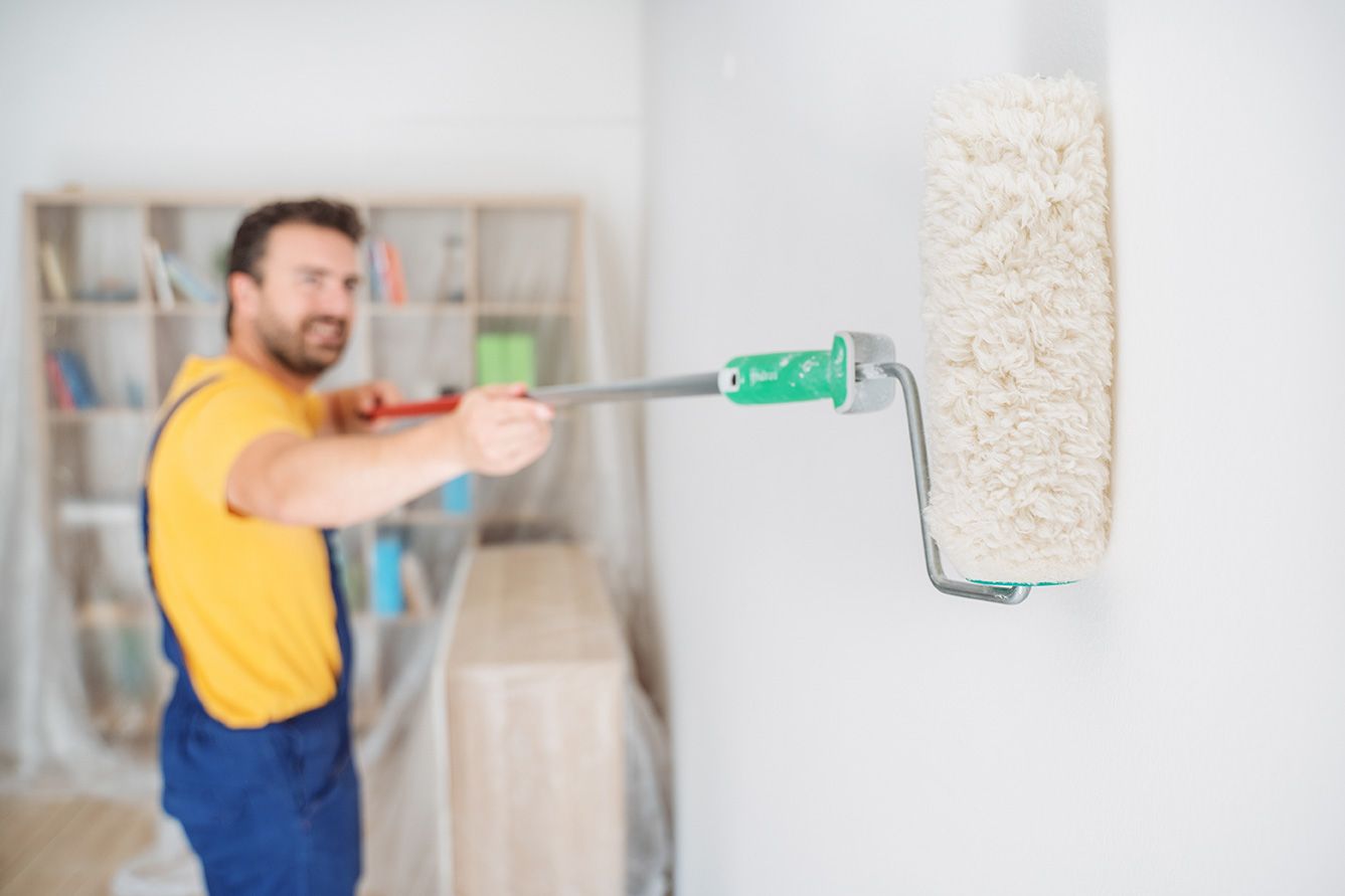 Un uomo sta dipingendo un muro con un rullo di vernice.