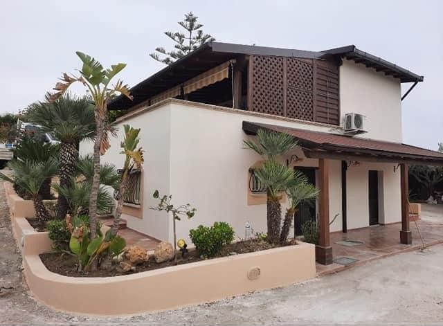 Una casa bianca con il tetto marrone è circondata da palme