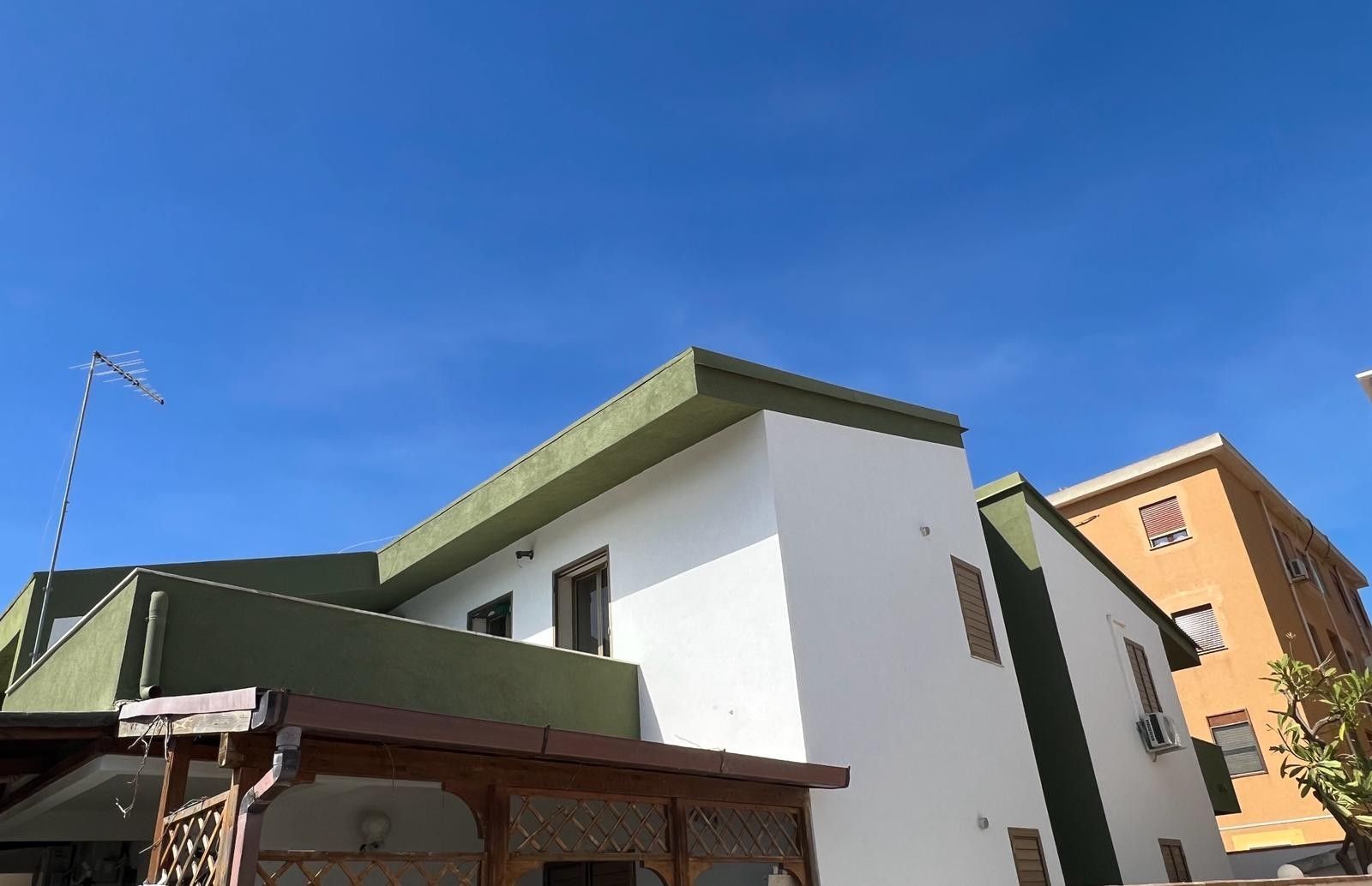 Una casa bianca con il tetto verde e un cielo azzurro sullo sfondo