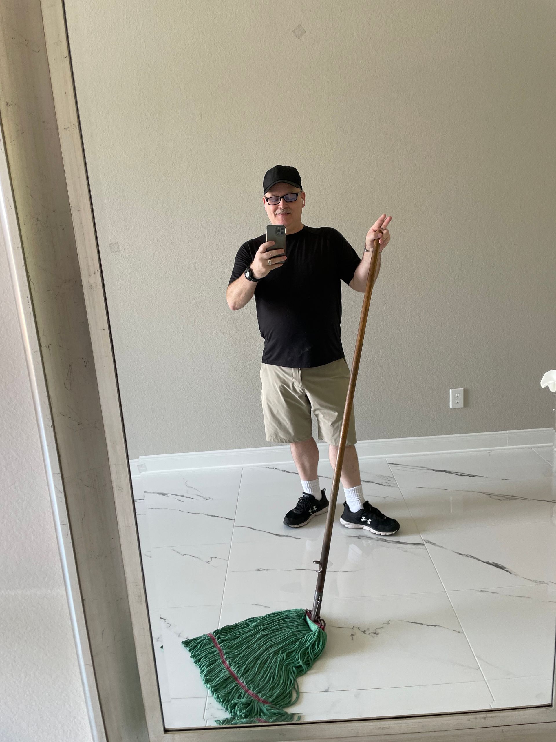 A man is taking a selfie with a mop in front of a mirror.