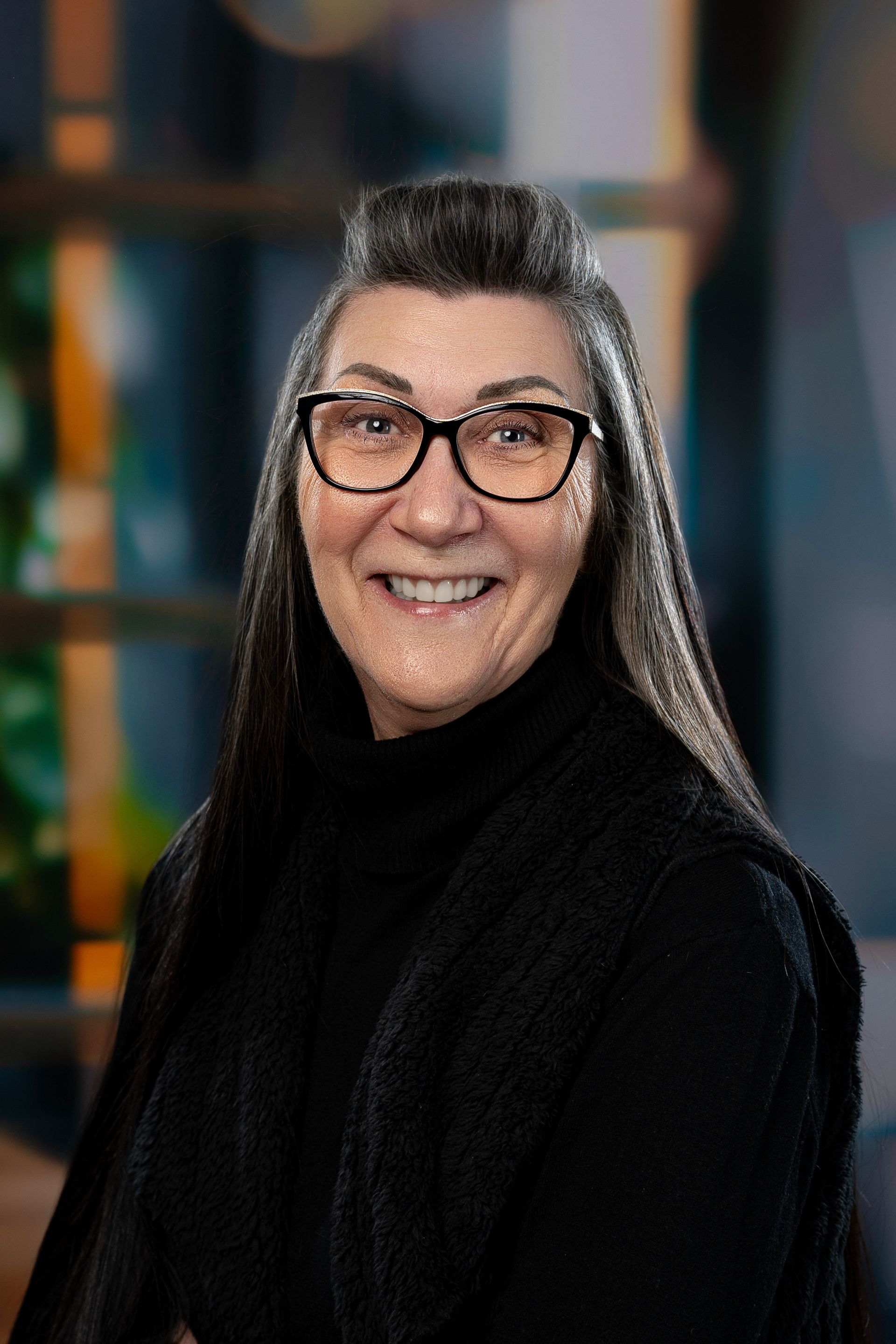 Une femme portant des lunettes et des boucles d'oreilles sourit à la caméra.