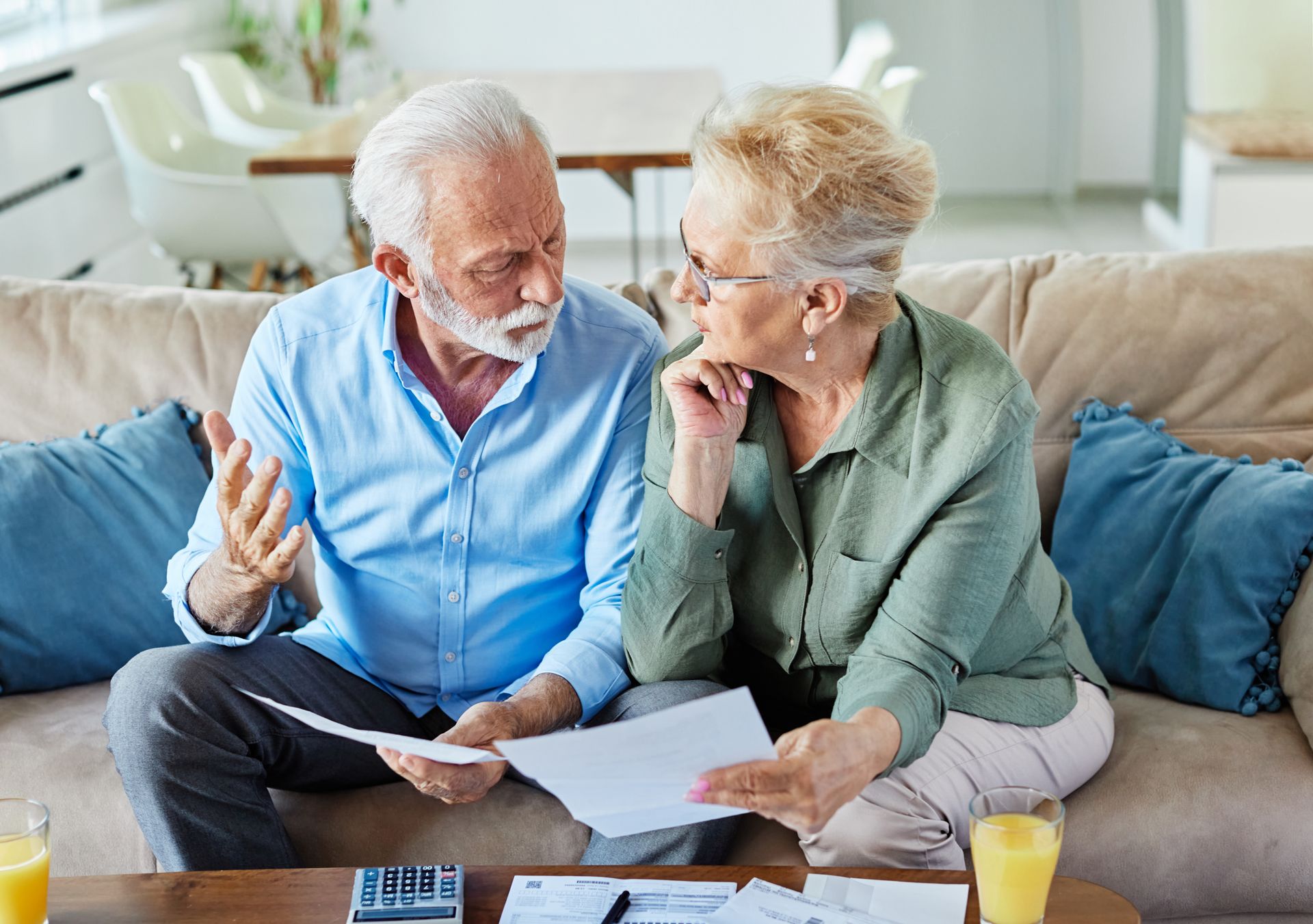 Un couple de personnes âgées est assis sur un canapé et regarde un morceau de papier.
