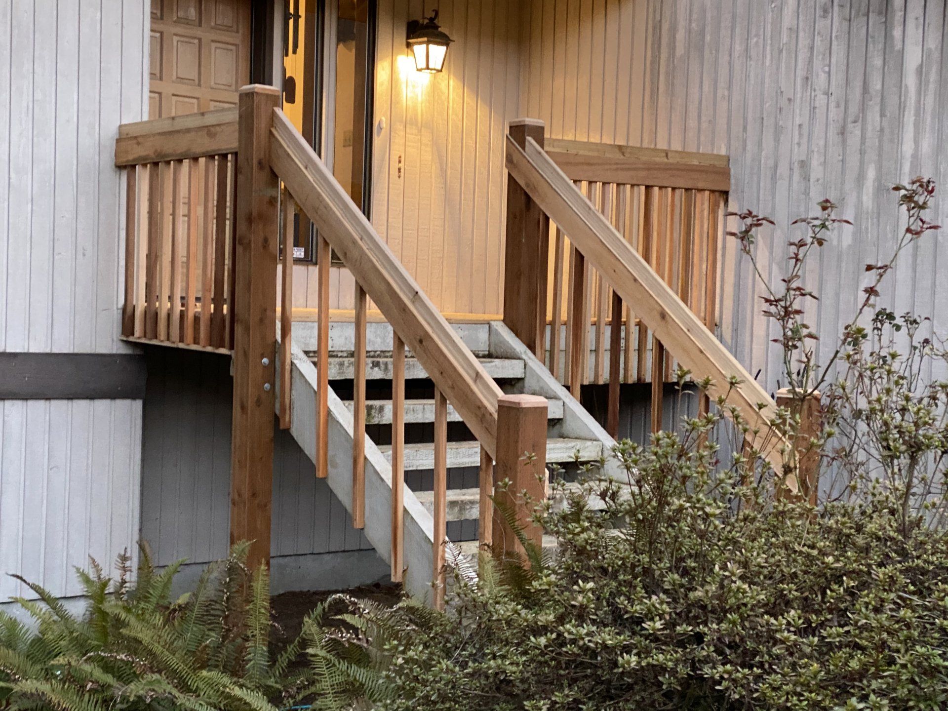 Wooden exterior staircase leading to a door, surrounded by railings. Plants are in front.