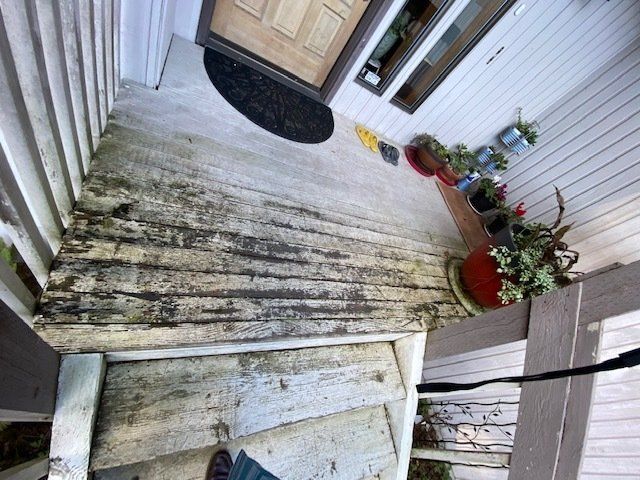 Weathered wooden porch with worn planks, steps leading down, potted plants, and front door.