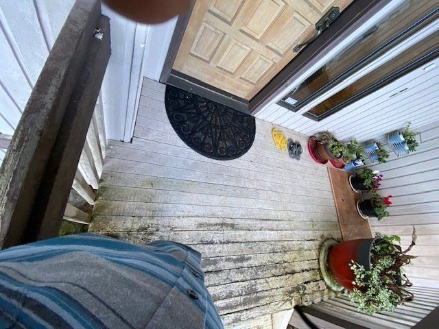 A porch with a wooden floor, plants, and a door, seen from a high angle.