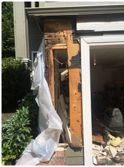 Damaged exterior wall of a building; rotted wood, missing siding, debris, and plastic sheeting.