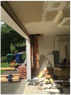 Garage undergoing renovation; debris on the floor, support beams exposed, view of yard outside.