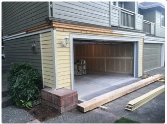Open garage with beige siding, wood beams, and a red brick base.