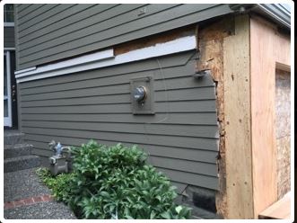 Damaged house siding with exposed wood frame, gas meter, and steps.