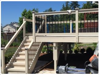 Beige deck with black railing, stairs, blue sky, and backyard.
