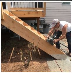 Man cutting a stair stringer on a deck with a saw, outdoors.