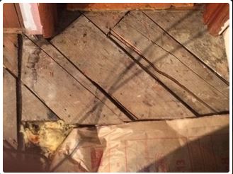 Wooden floorboards in an attic, some angled, with insulation visible below.