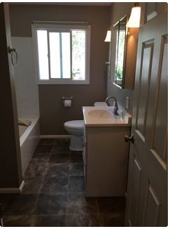 Bathroom with a white vanity, toilet, and bathtub. The walls are gray, and the floor is dark tile.
