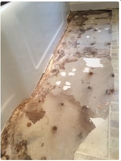 Damaged bathroom floor with peeling paint and water stains near bathtub.