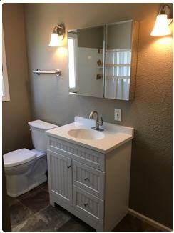 Bathroom with white vanity, toilet, and beige walls. Two sconces and a mirrored medicine cabinet are mounted.