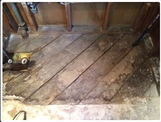 Diagonal wooden floorboards, damaged, exposed plumbing, in a room under construction.