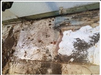 Close-up view of a damaged, crumbling wall with dirt and discoloration, possibly water damage.