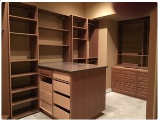 Empty, newly built walk-in closet. Brown cabinetry with shelves, drawers, and center island with granite countertop.