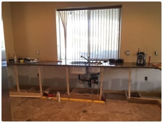 Kitchen renovation with a dark countertop and sink. Wooden supports under the counter, unfinished.