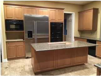 Kitchen with light wood cabinets, stainless steel refrigerator, and granite island countertop.
