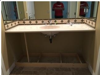 Bathroom sink under construction, with a beige countertop and beige tile. A person is in the mirror's reflection.