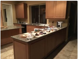 A kitchen with light brown cabinets, a granite countertop island, and various items on the counter.