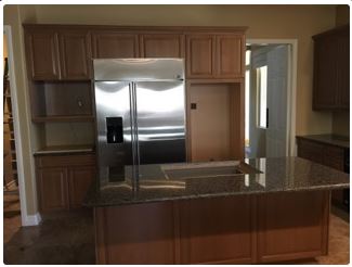 Kitchen with wood cabinets, stainless steel fridge, and island with granite countertop.