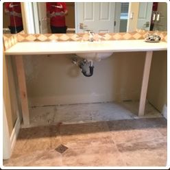 Bathroom sink with open space below, supported by two wooden legs. Beige countertop and tiled floor.