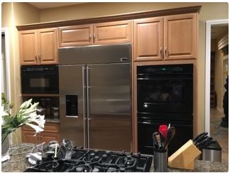 Kitchen with stainless steel refrigerator, black oven, and light wood cabinets.
