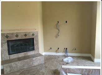 Empty living room with fireplace and wall outlets. Tan walls, stone tile surround the fireplace.